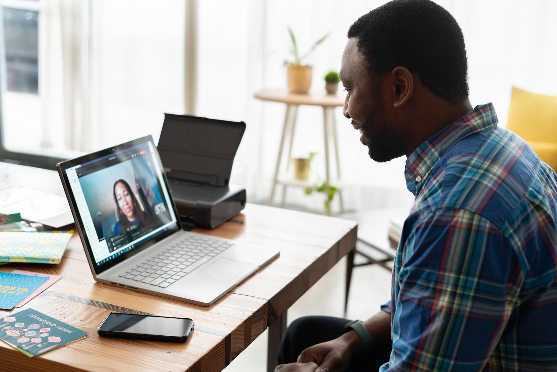 man of color sitting at table on meeting on laptop